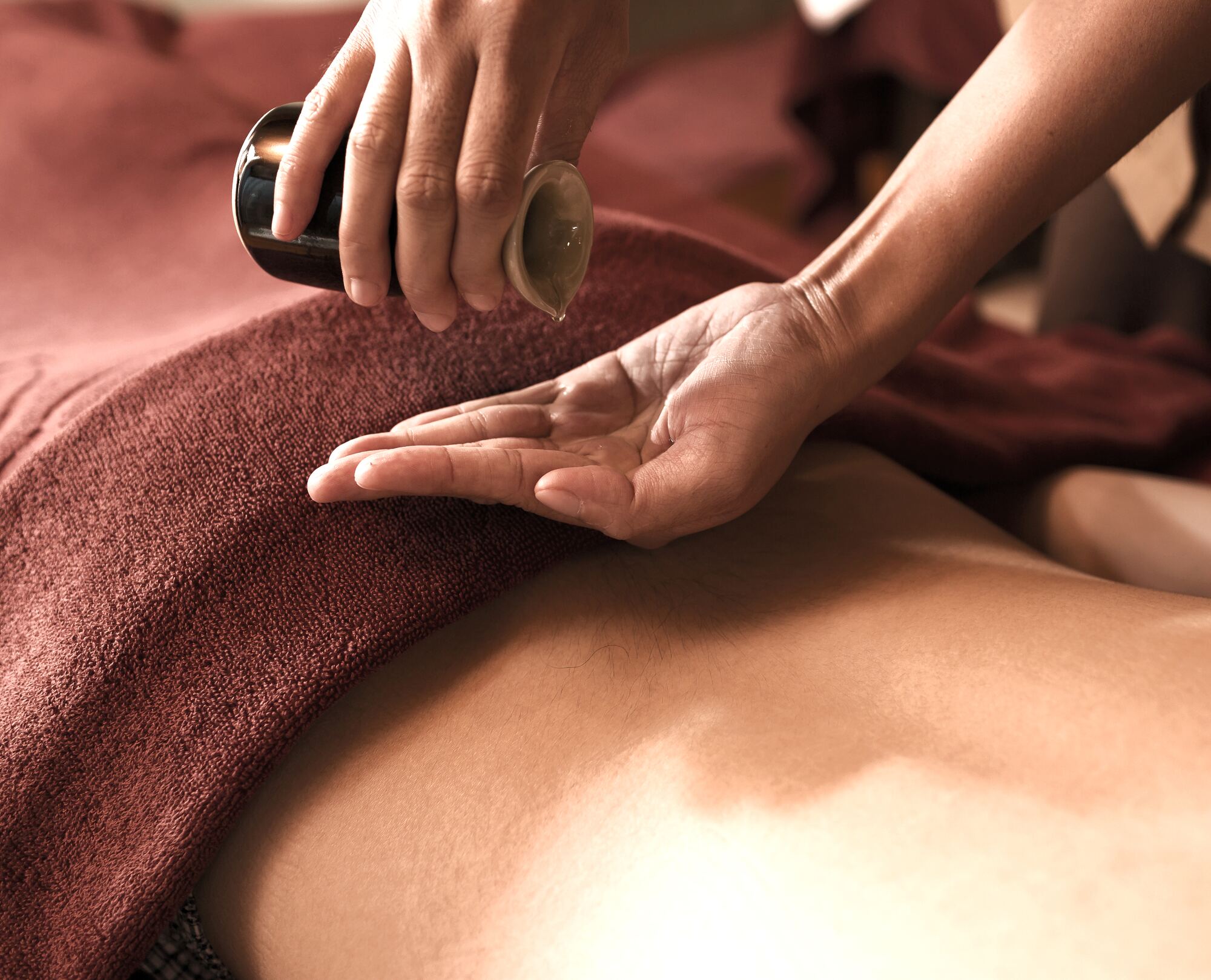 Masseur giet warme aroma-olie in de hand boven de rug van een cliënt